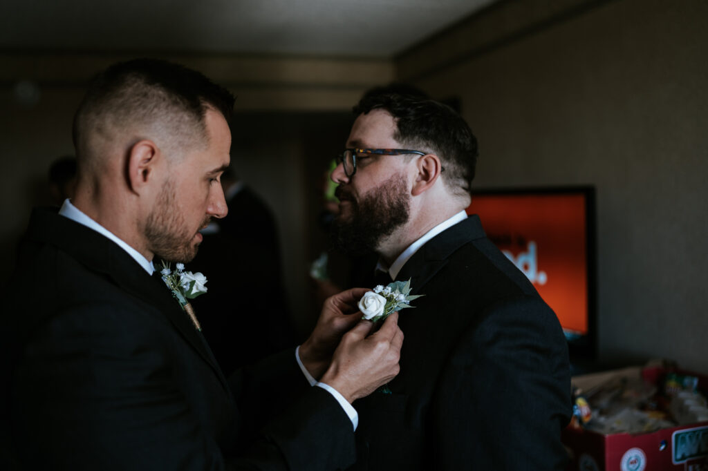 Groom is pinning a boutonnière on one of his groomsmen  